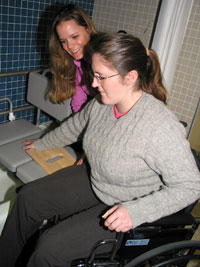 Hanna instructs and assists in the use of a sliding board that is used to tranfer a patient from a wheelchair to a bath bench.